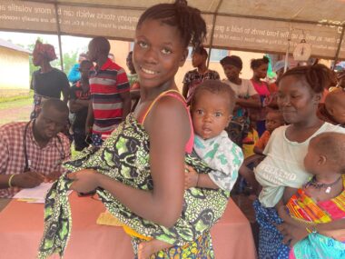 PHOTO-2024-07-10-07-43-01 The village of Fengehun gathered for care under tent with woman who has baby wrapped on her back
